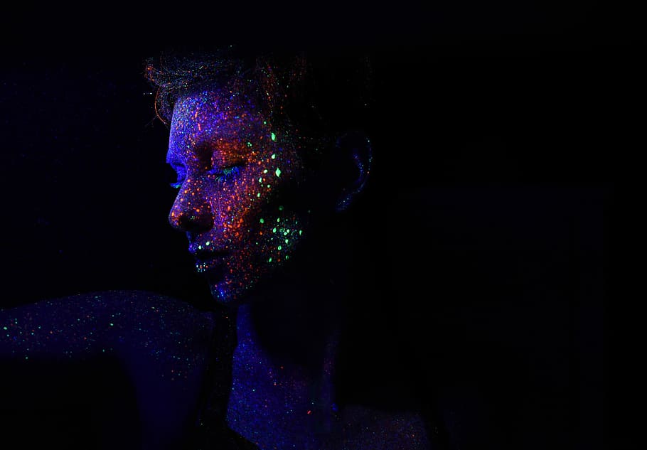 person in dark background with galaxy effects on face, man with glow in the dark paint splattered on face