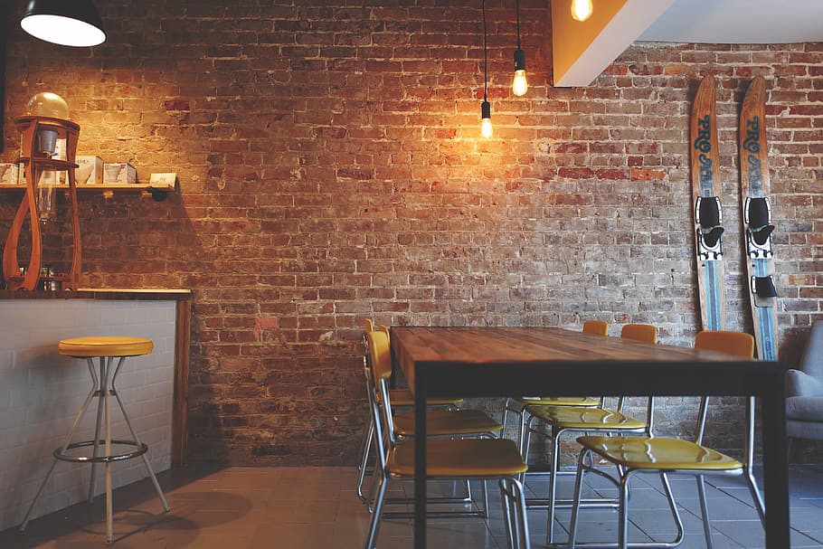 brown wooden dining table with yellow padded chairs near brick wall \