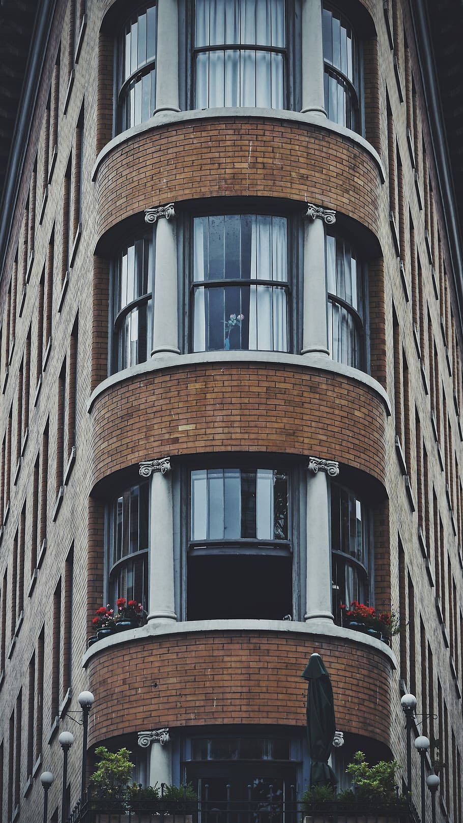 brown and white concrete building, red petaled flowers in balcony of brown bricked building at daytime HD wallpaper