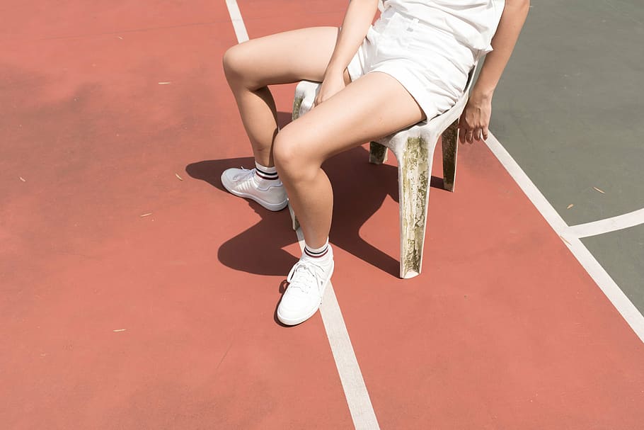 person wearing white shorts sitting on plastic chair beside green court
