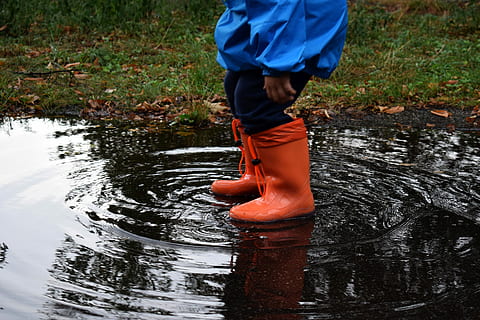 child wearing orange rain boots stepping on body of water at daytime HD wallpaper