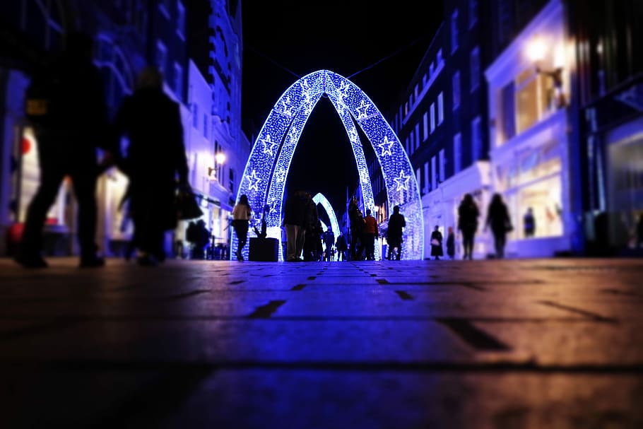 people walking near arched lighted decor between buildings, people walking toward blue and white star print pathway during night time HD wallpaper