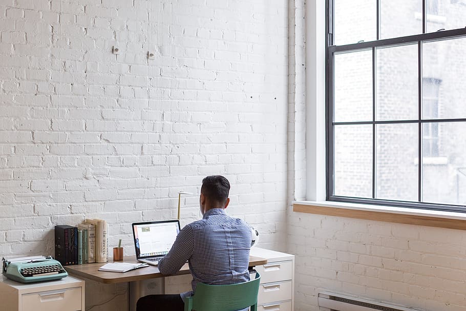 man sitting on green chair while using his laptop near the window HD wallpaper