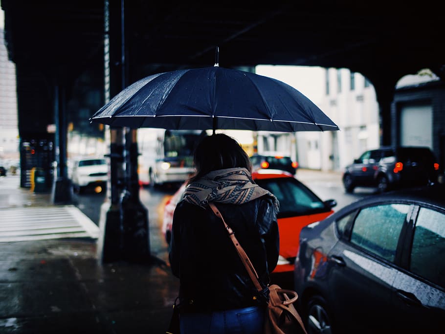 woman holding umbrella walking on street during daytime, woman holding umbrella while walking on street