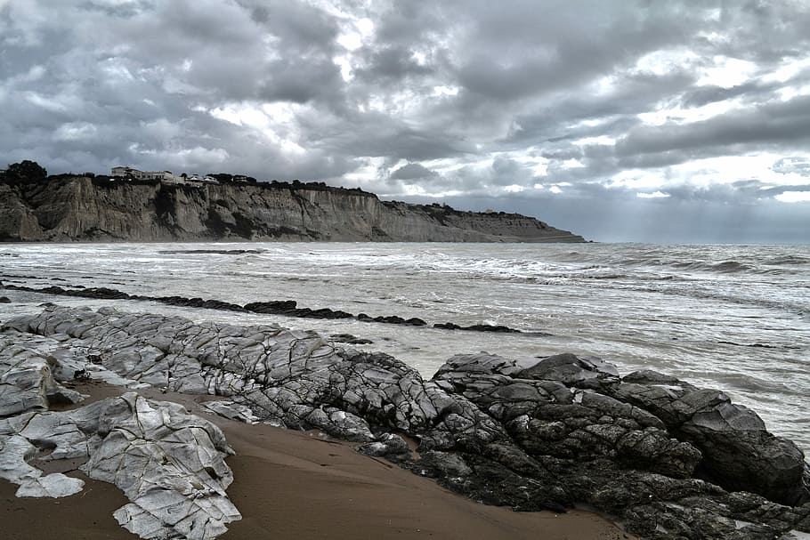 grey rocks near sea under grey sky, seashore beside mountain HD wallpaper