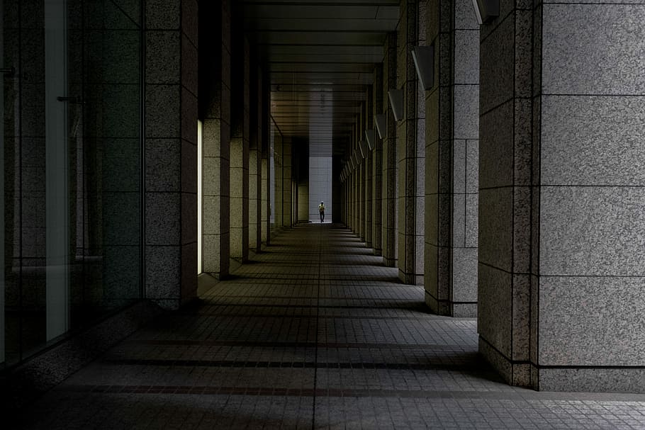 person standing on hallway, person standing between gray concrete pillars of building architectural photography HD wallpaper