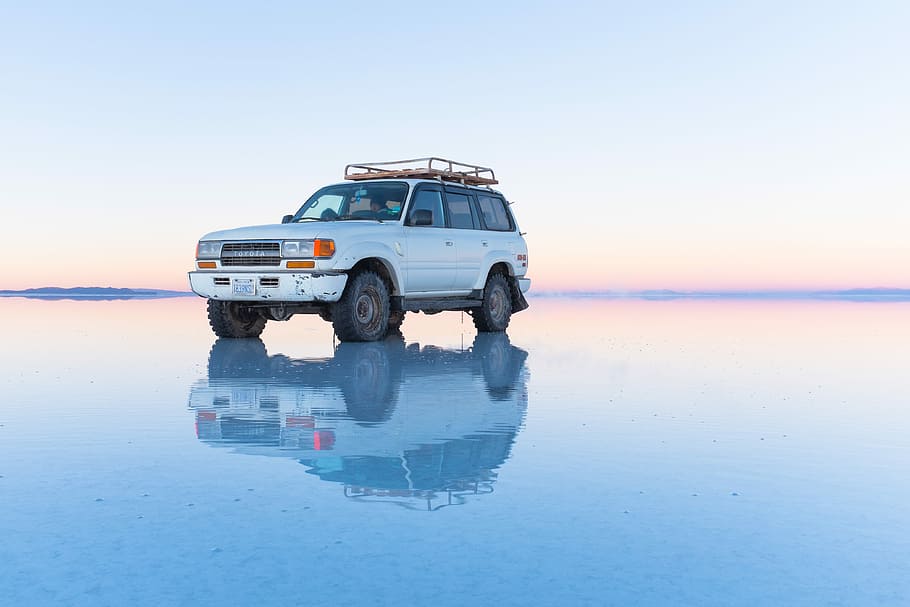 white SUV parked on body of water, white Nissan Patrol on salt flats under white clouds