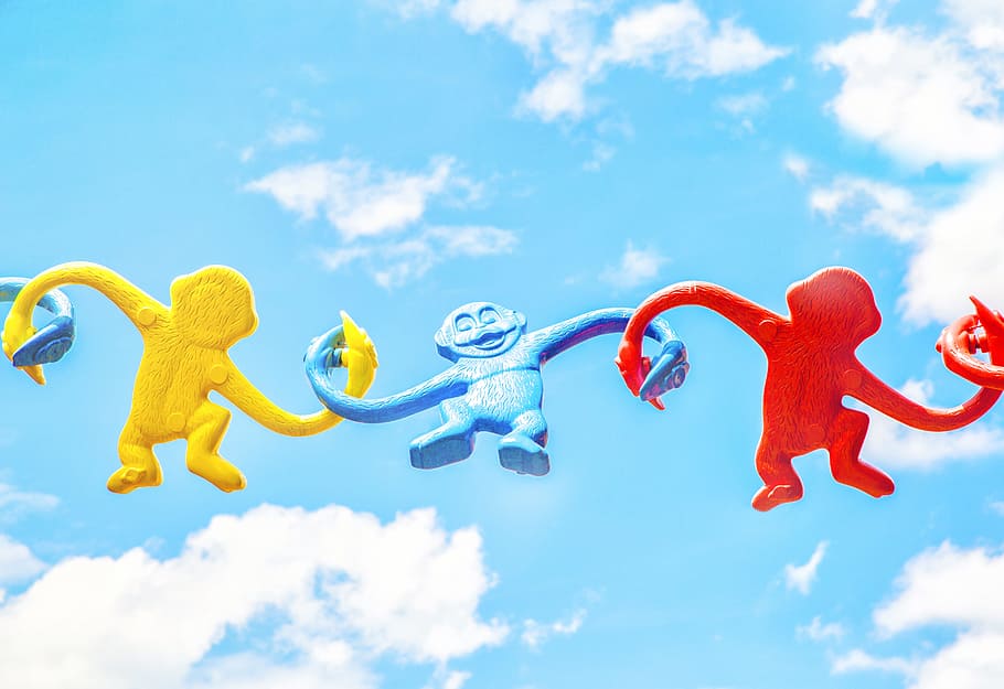 three assorted-color monkey plastic toys holding each other during daytime, three red, blue, and blue primate figurine