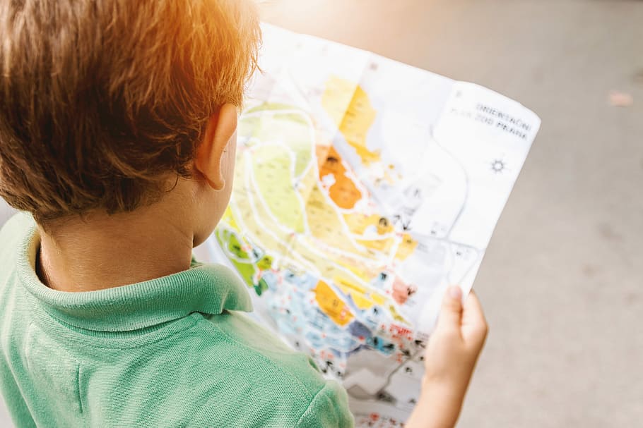 boy standing while reading map, boy wearing green polo shirt holding map illustration