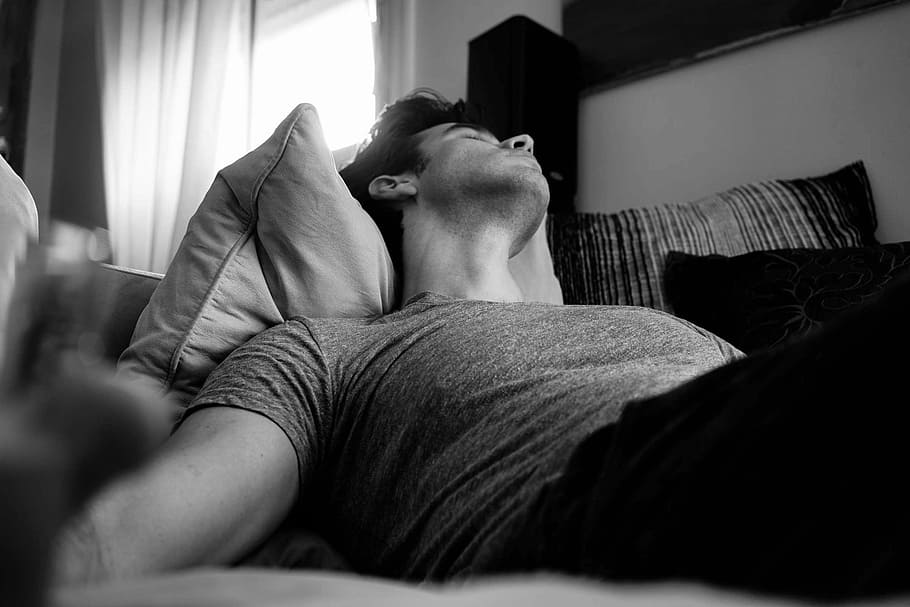 grayscale photo of man laying on bed, man lying on pillow, nap