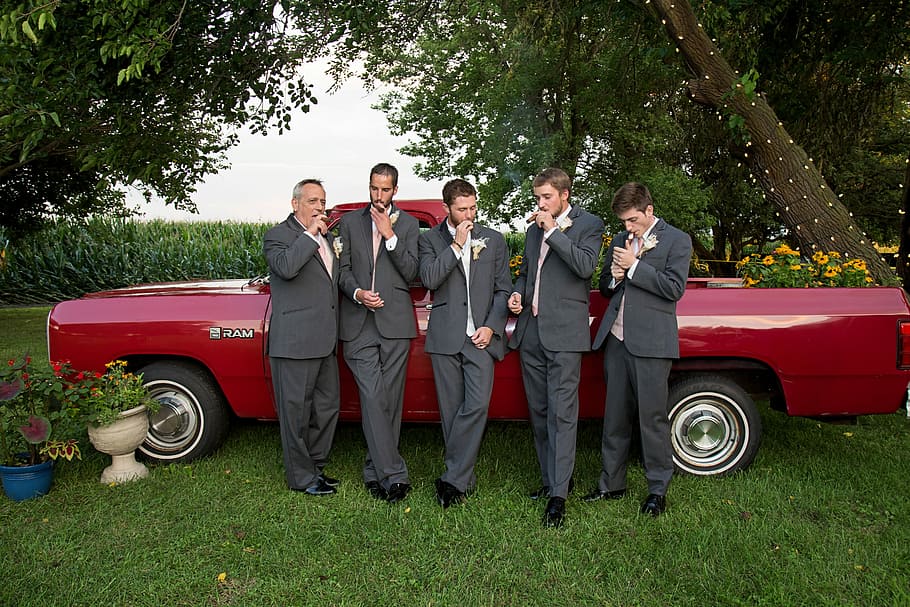 group of men in wedding photo shoot with red car on background